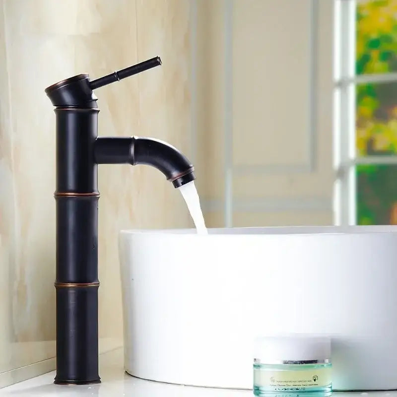 Black bamboo-style high arch mixer faucet with bronze accents flowing water into white bathroom sink
