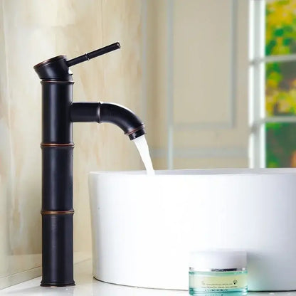 Black bamboo-style high arch mixer faucet with bronze accents flowing water into white bathroom sink