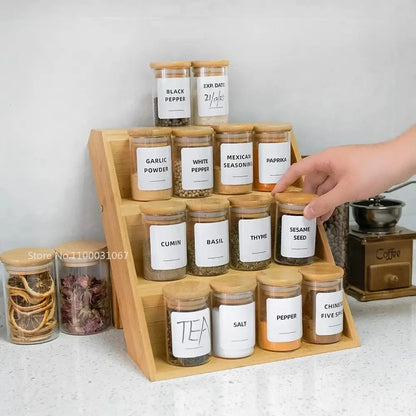 Wooden spice rack holding clear glass food storage jars with bamboo lids and white labels for kitchen use