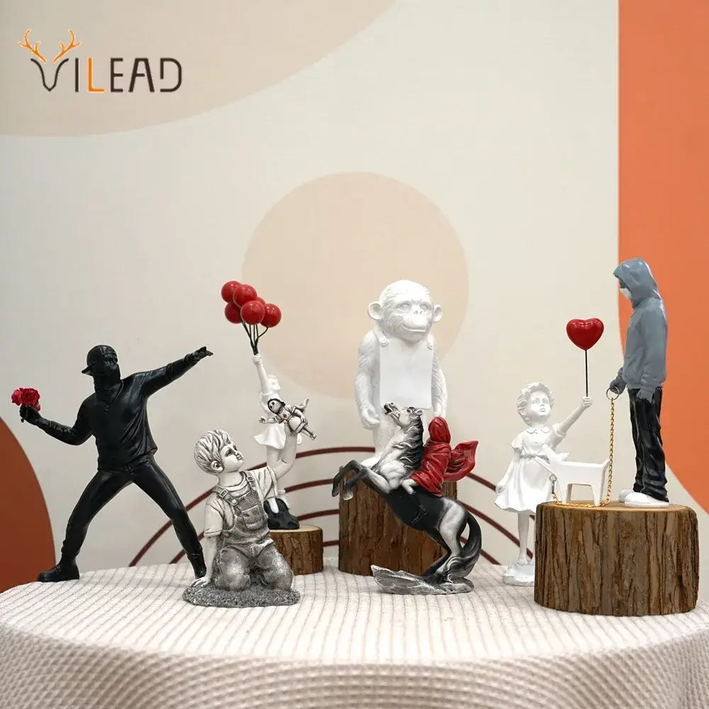 A banksy sculpture collection of black and white resin figurines featuring a masked figure with roses and balloon girl figurines