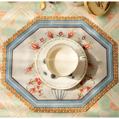 White ceramic teacup with gold rim and floral pattern on matching saucer with decorbites baroque flowers fringe placemat set
