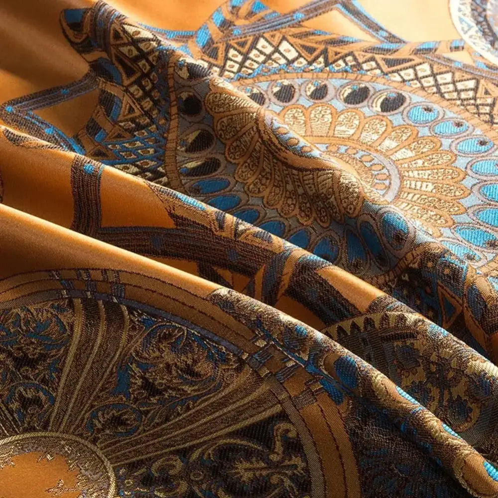 A luxurious golden-orange silk scarf with intricate blue and black patterns complements decorbites golden jacquard bedding set