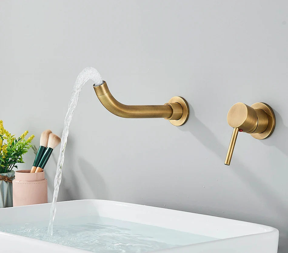 Gold-toned wall-mounted basin faucet with brushed brass finish curved spout and separate hot water control handle