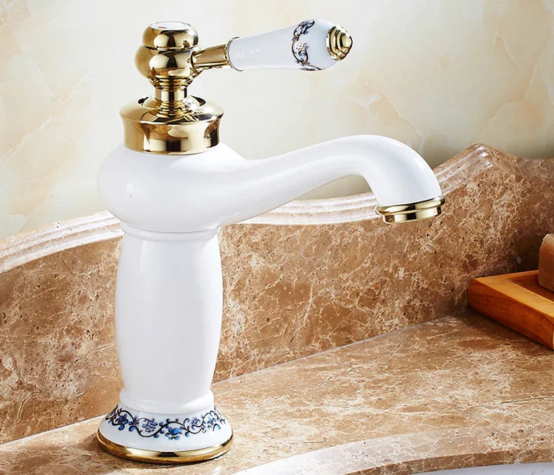 White ceramic bathroom faucet with antique bronze finish gold accents and blue floral detailing on handle and base