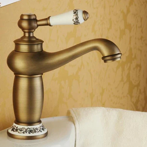Antique brass-finished bathroom faucet with a bronze finish white ceramic handle and black floral patterned base