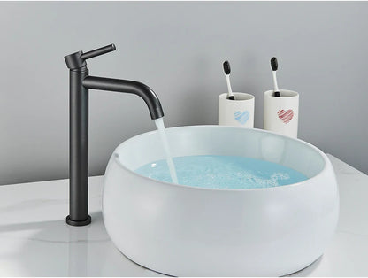 Black matte finish tall bathroom faucet with curved spout flowing water into white ceramic vessel sink