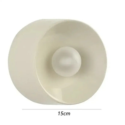 Cream-colored translucent plastic candle holder with spherical base and flared rim complementing bauhaus metal wall lamp