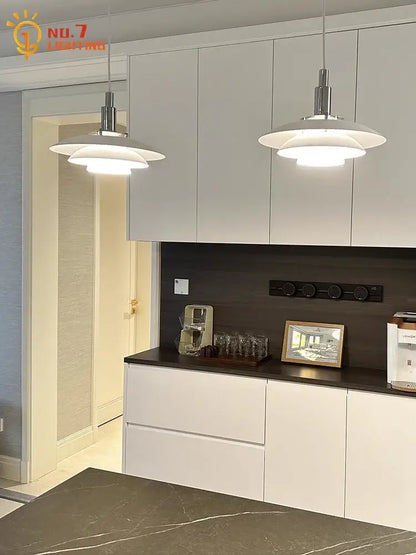 Two sleek white bauhaus flying saucer pendant lights with polished chrome fixtures hang above a kitchen island