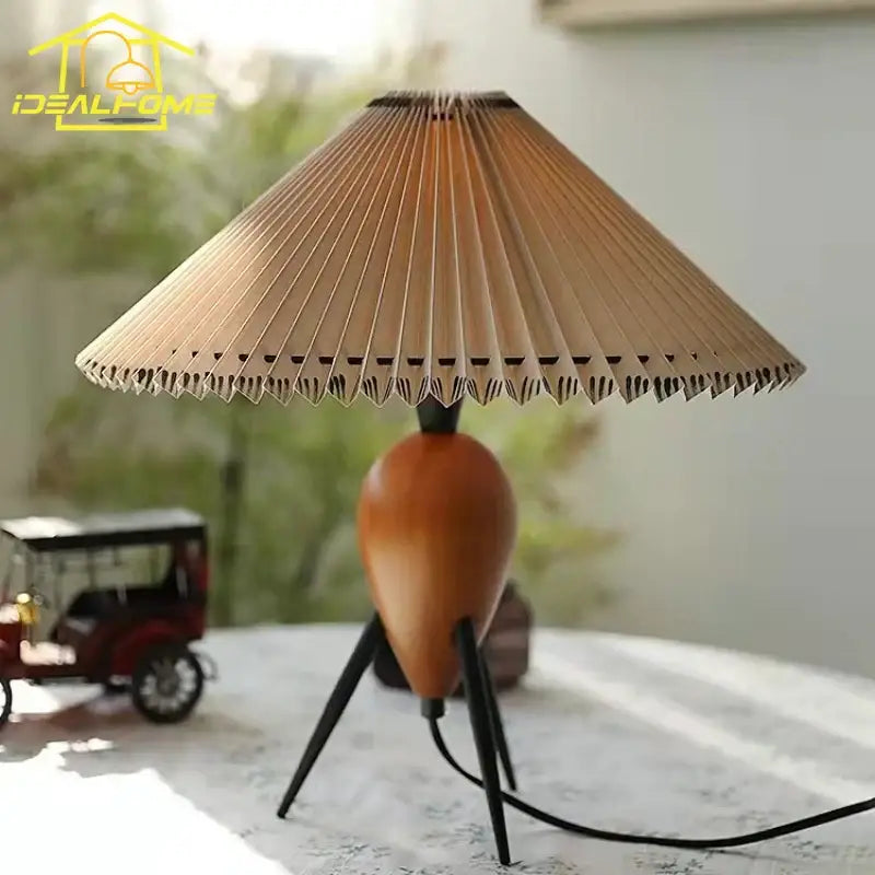 A warm-toned bauhaus pleated wood table lamp with accordion-style shade and tripod base for bedroom or desk use