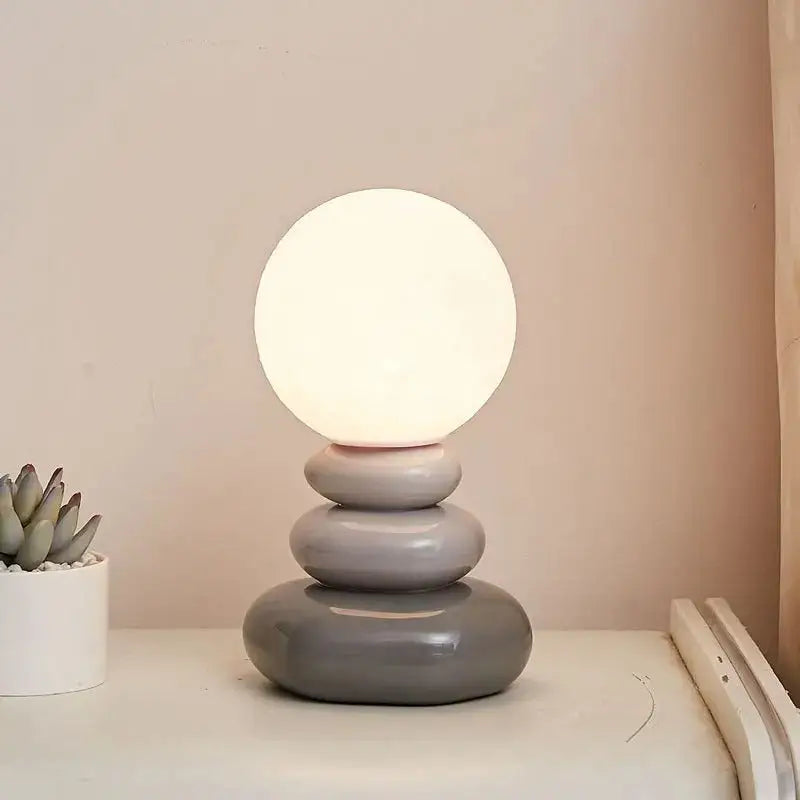 A bauhaus table lamp with a glowing white spherical bulb on stacked glossy gray ceramic rings