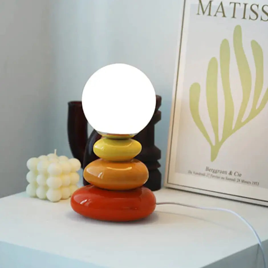 A modern bauhaus table lamp with stacked ceramic rings in orange yellow and red hues with glossy finish