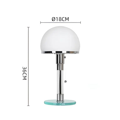 A bauhaus glass ball desk lamp with frosted white spherical shade and chrome stem on a clear base for bedroom use
