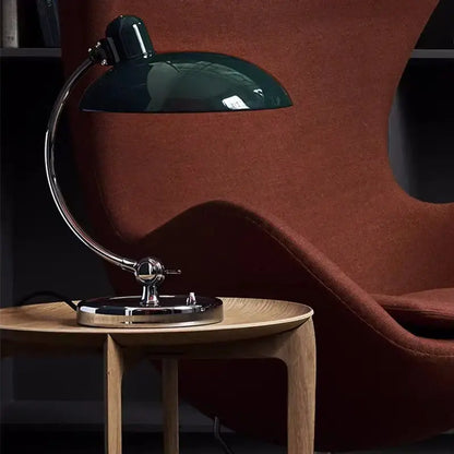 A sleek dark green bauhaus vintage desk lamp with chrome base and articulated arm on wooden side table