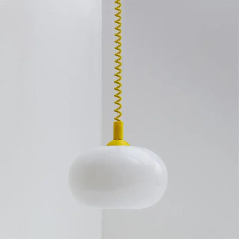 A bauhaus glass pendant light with sleek white opal glass and vibrant yellow coiled cord for dining room lighting