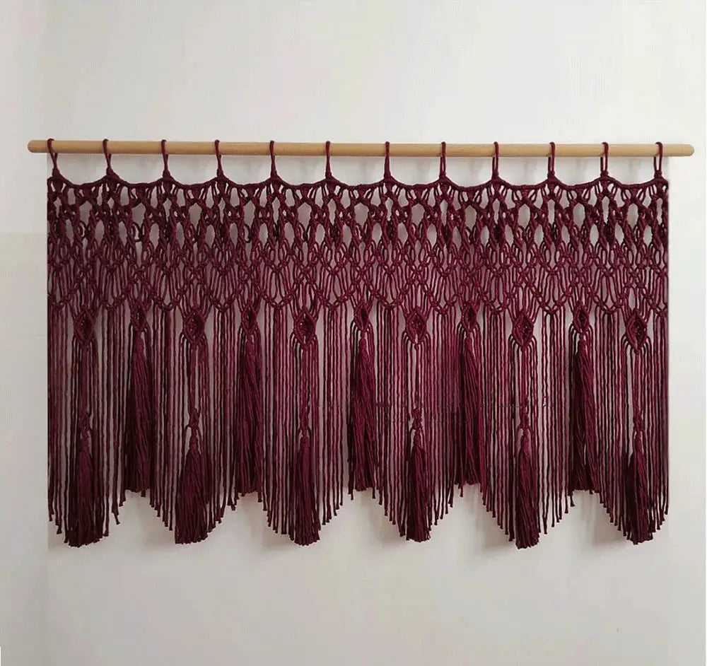 A maroon decorbites handwoven macrame wall hanging with intricate knotwork and tassels suspended from a light wood rod