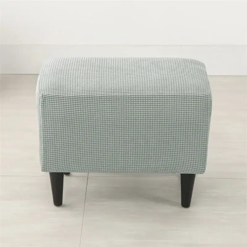 A light blue upholstered ottoman with a subtle grid pattern and dark wooden legs for velvet plush recliner cover use