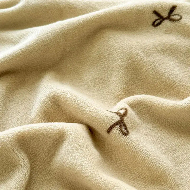 Beige scalloped cozy coral fleece blanket with cream-colored plush texture and brown embroidered bows for decorbites cozy coral decor