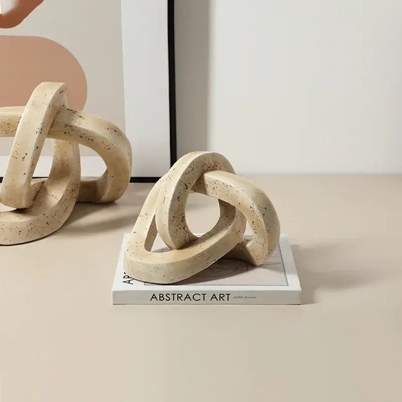 Cream-colored speckled ceramic bookends featuring a geometric interlocking loop knot design for living room decor
