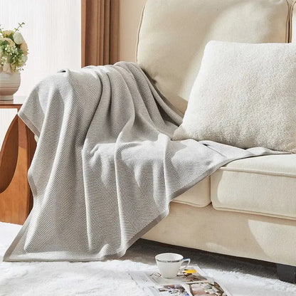 Beige and tan herringbone knit blanket by decorbites draped over a sofa arm in a living room setting