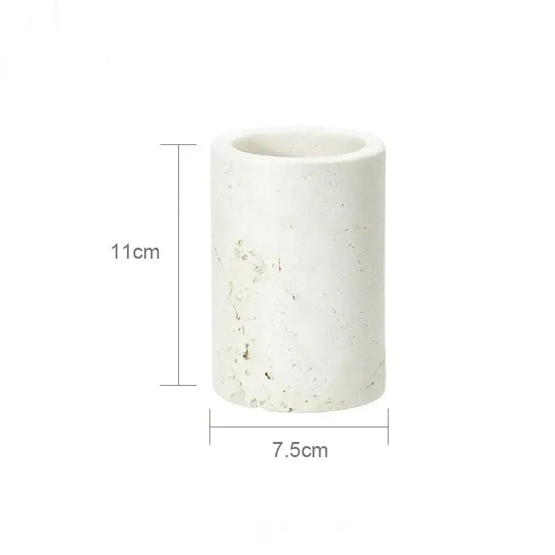 A cylindrical white concrete planter with a textured speckled surface in a beige travertine marble bathroom set