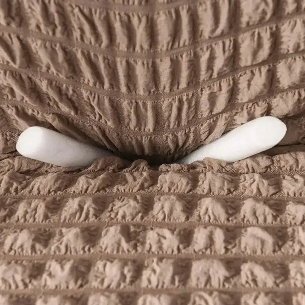 Beige waffle cozy sofa cover with elastic edges and solid color design shown with two white cylindrical objects underneath
