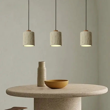 Three beige columnar micro cement pendant lights with wood accents hang above a stone table for kitchen decorbites decor