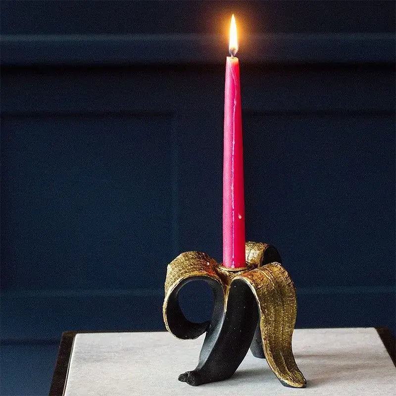 A vibrant pink candle in a decorative black and gold metallic banana candlestick holder for dining room decorbites golden banana decor