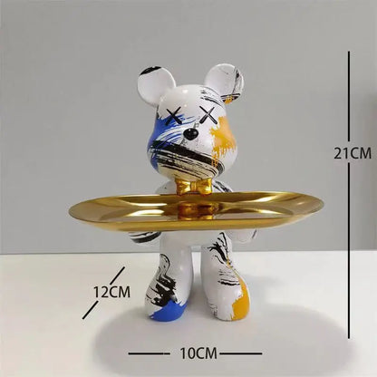 White bear figurine with blue black and yellow paint splatters and x shaped eyes holding a gold tray decorbites graffiti bear