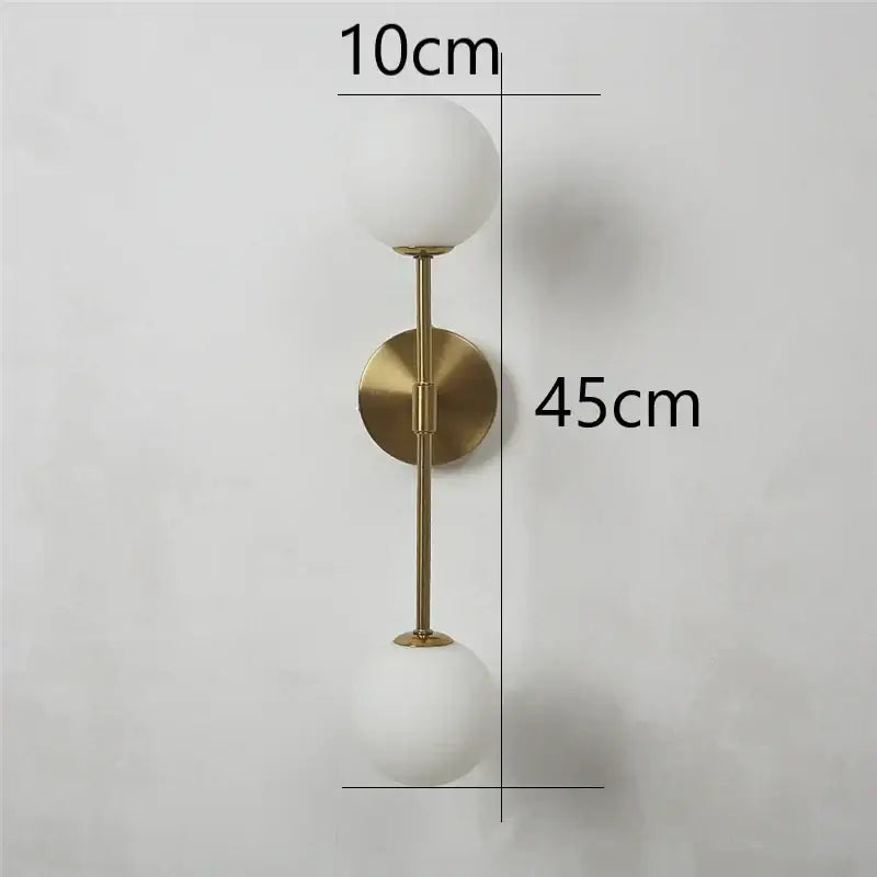 A modern black and golden glass wall lamp with brushed gold finish and two frosted white spherical shades for bedroom decorbites golden glass led