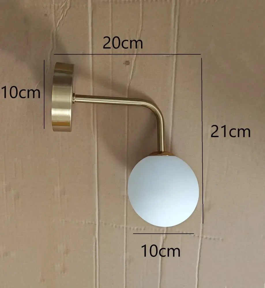 A sleek brass-finished decorbites golden glass led wall lamp with frosted white spherical shade for bedroom sconce