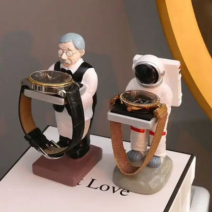 Two whimsical watch holders shaped like a vintage waiter and astronaut beside a black and iridescent purple cartoon bear watch stand bedroom decor