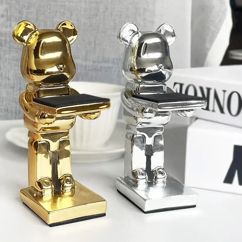 Two glossy gold and silver cartoon bear watch stand phone holders with black trays for bedroom decor