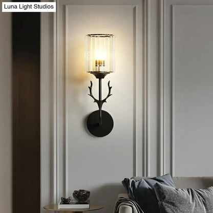Black metal wall sconce with antler-inspired design and clear glass cylinder housing three warm-toned e26 e27 bulbs
