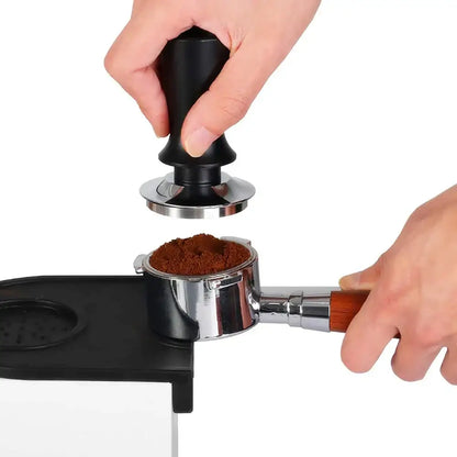Black calibrated espresso coffee tamper with silver metal base and wooden spring handle pressing coffee grounds