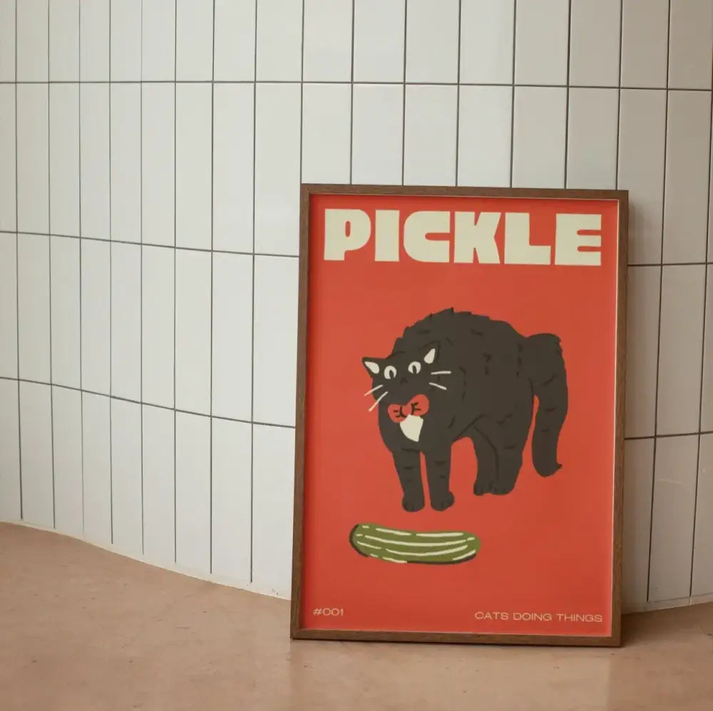 A framed decorbites™ canvas wall art with a bold red background featuring a funny black cat holding a pickle