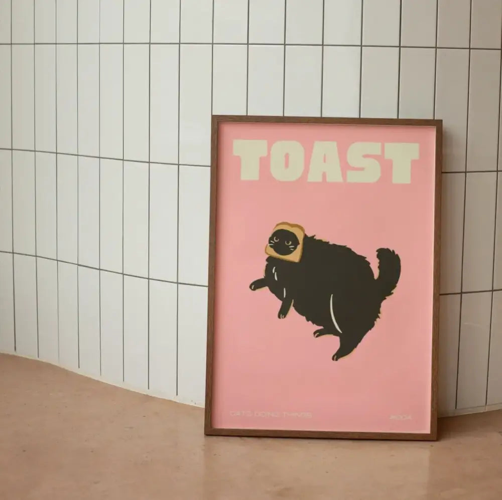A framed wall art canvas featuring a black cat with a toast slice on its head and the word toast in bold white letters