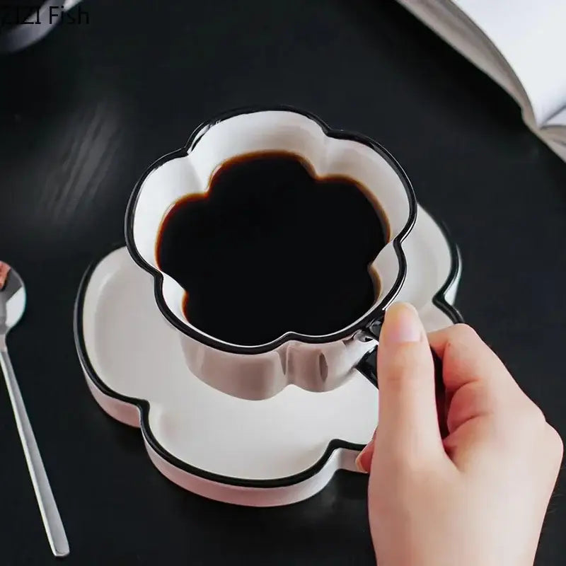 A white ceramic cup with black edged flower petal design filled with dark coffee from a black edged mug set