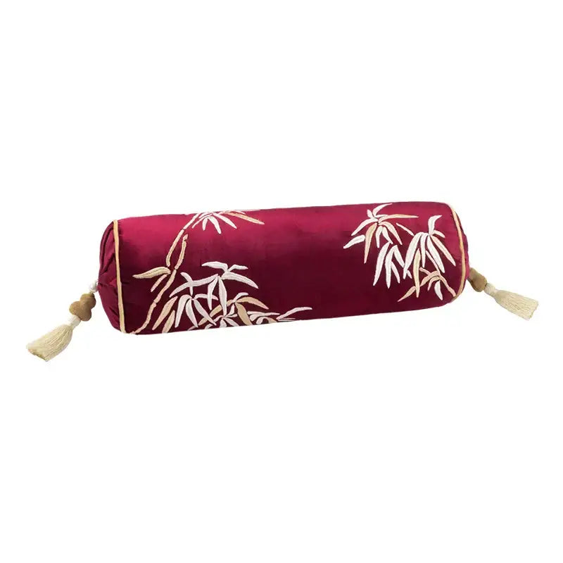 A deep red bolster pillow cover with white and beige bamboo leaves embroidery and matching tassels for bedroom decor