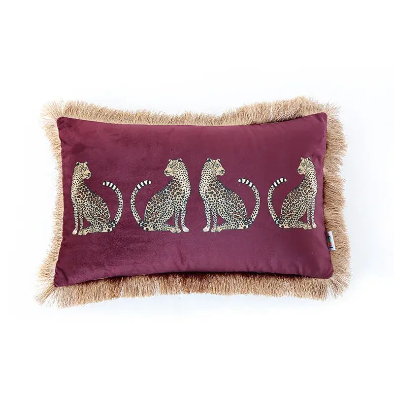 A maroon velvet throw pillow cover with embroidered leopard silhouettes and tan fringe tassels for living room decor