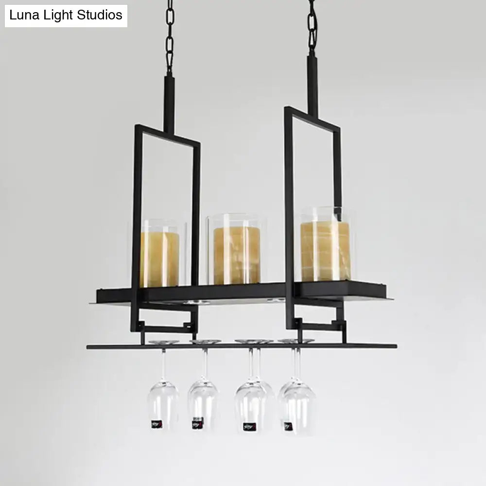 Decorbites black metal wine rack with glass candle holders and hanging wine glasses beneath clear glass cylindrical island light fixture