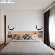 Black metallic antler sconce wall mounted lighting fixture symmetrically mounted above the bedroom bed