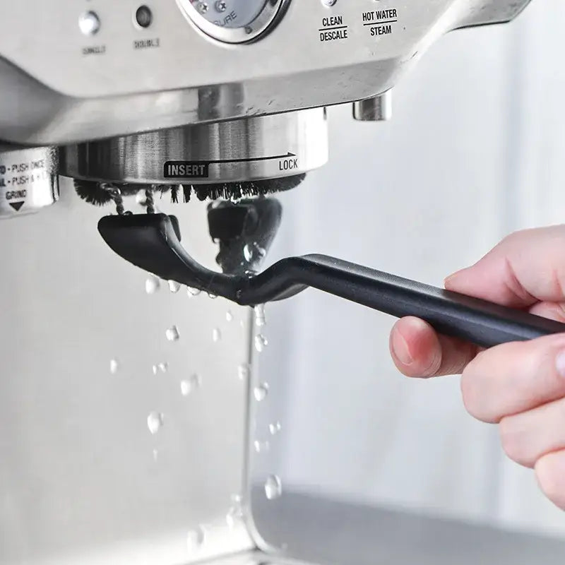 Black plastic coffee machine grinder brush with bristles cleaning the spout of a stainless steel decorbites coffee machine