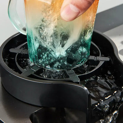 A gradient-colored glass mug with orange to teal textured surface near a black plastic glass rinser faucet accessory