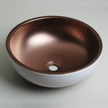 A hand painted ceramic vessel sink set with a white exterior and polished copper interior for bathroom use