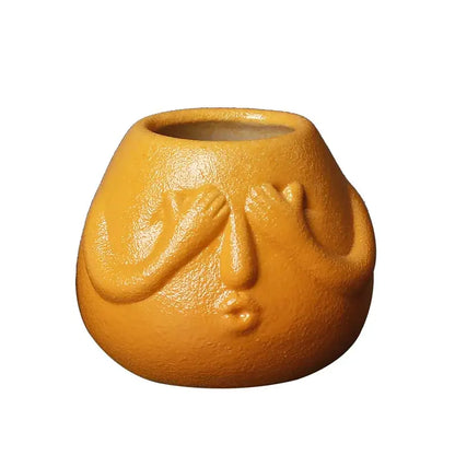 A matte orange ceramic abstract human face planter with hands covering eyes for decorbites ceramic abstract decor