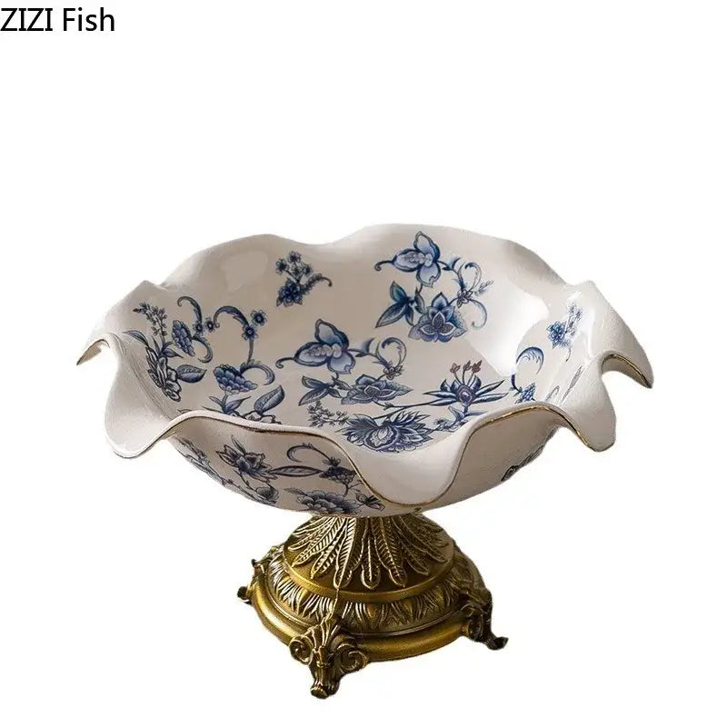 White ceramic fruit bowl with blue flower pattern footed design and gold-trimmed scalloped rim on ornate gold base