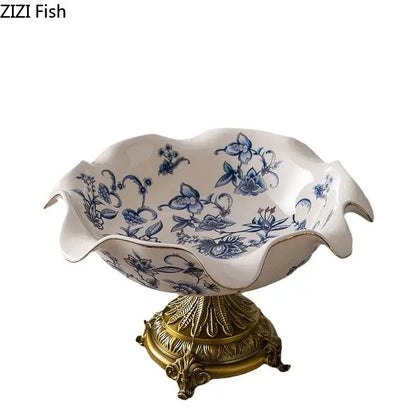 White ceramic fruit bowl with blue flower pattern footed design and gold-trimmed scalloped rim on ornate gold base
