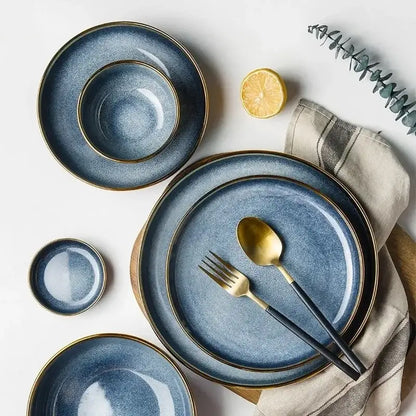 Blue gradient ceramic plate set with gold rims paired with black-handled cutlery for elegant dining room use