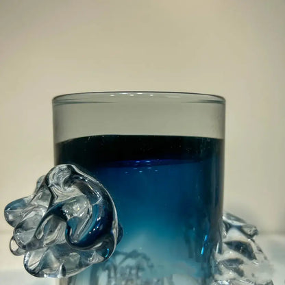 Clear glass mug with a sculpted transparent handle resembling an abstract hand and blue gradient wavy vase decor