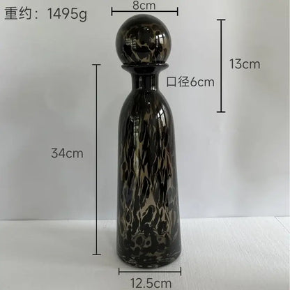 A tall glossy black glass decanter with swirling gold and dark leopard print glass vase design and a spherical stopper decorbites leopard print